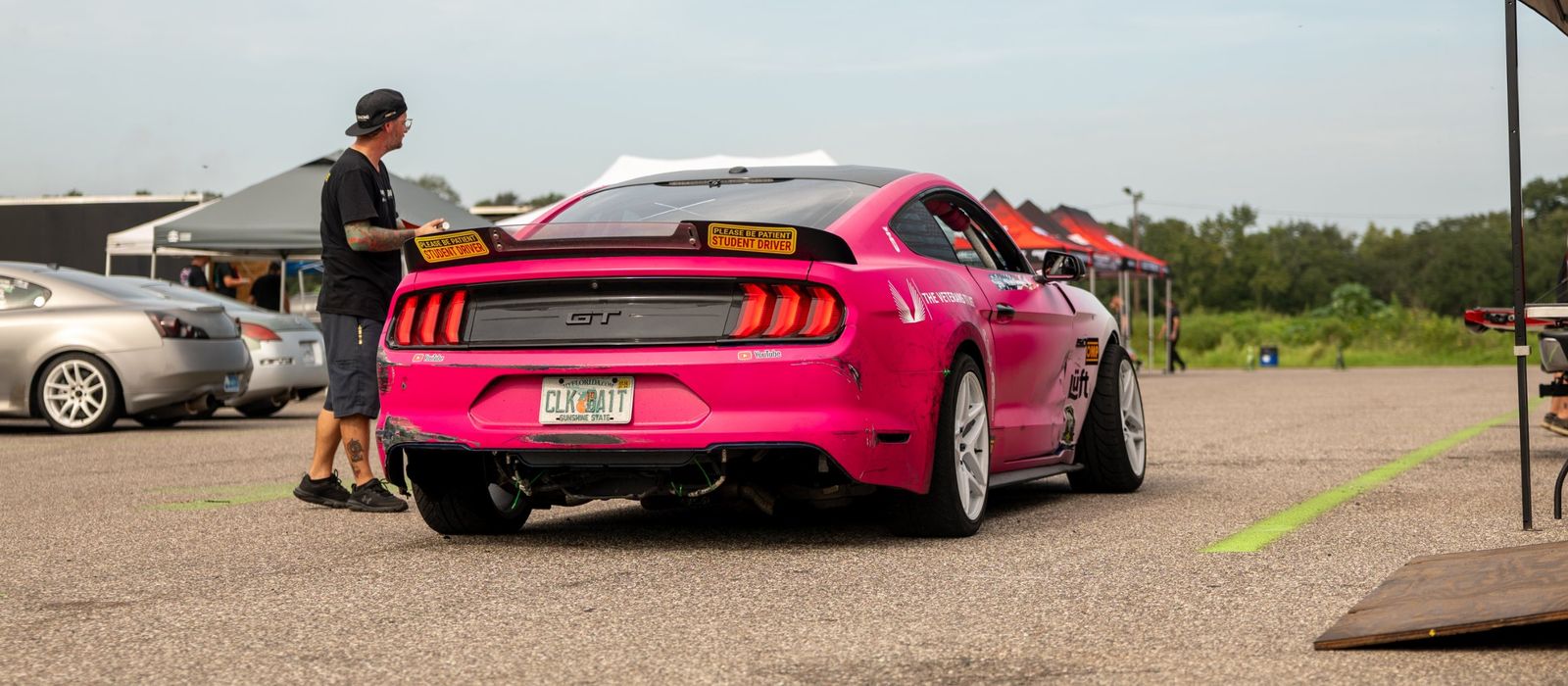 The pink #16 Mustang from behind in the paddock, with student driver stickers on the wing